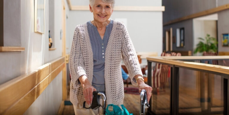 Smiling Elderly Woman Walking Safely with a Walker in the Hallway at Assisted Living Facility